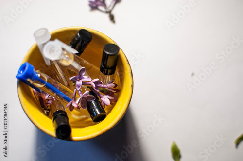 Canvas Print Creative composition of perfume sample vials and purple lilac flowers inside a b