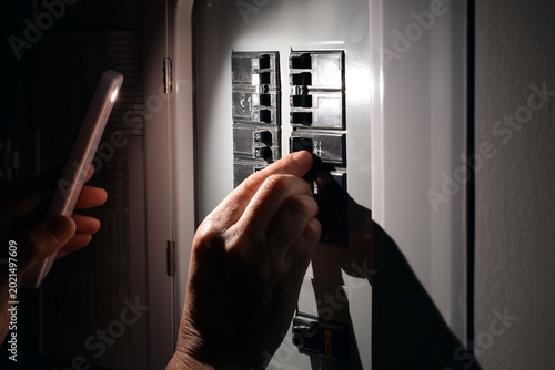 Foto Closeup of person using smartphone flashlight while switching electrical circuit breakers in dark home