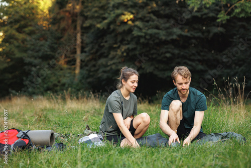 Young couple setting up a tent in forest at summer