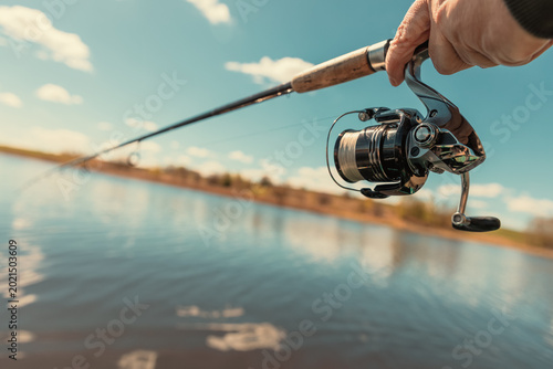 A fishing rod with a spinning reel in the hands of a fisherman on a spring day. Fishing background.