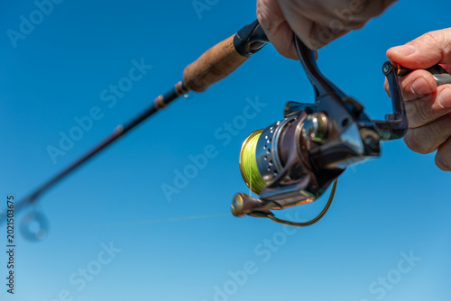 A fishing rod with a spinning reel in the hands of a fisherman on a spring day. Fishing background.