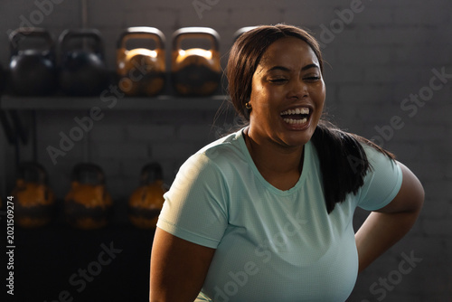 Bild auf Leinwand African American woman laughing, catching breath in gym wearing light blue shirt