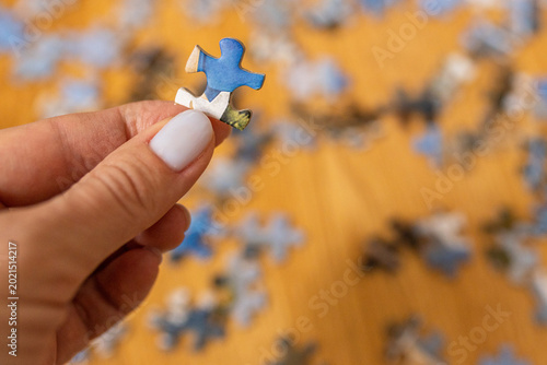 Woman holding a single puzzle piece above a wooden table with scattered jigsaw pieces. Strategy, problem-solving, and finding a solution. Mental leisure and hobby development concept.