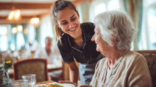 Friendly Young Nurse Serving Meal to Senior Woman in Nursing Home Restaurant, Professional Caregiver Smiling at Elderly Patient During Lunch, Compassionate Healthcare and Senior Care Concept