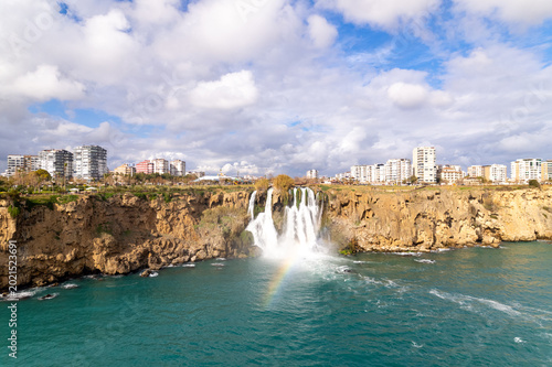 Foto Düden Waterfall pours dramatically into the turquoise Mediterranean Sea beside Antalya’s coastal cliffs under textured clouds and vibrant natural scenery