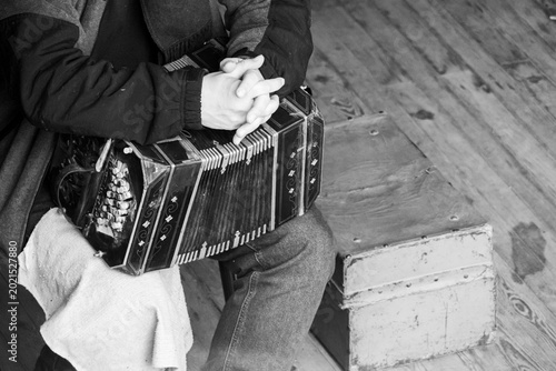 High-angle close-up shows hands on a bandoneon. Monochrome highlights intricate details.