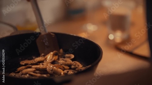 Inside bustling kitchen, chef-man sautes fresh champignons in hot pan, the sizzling mushrooms releasing earthy aromas as he skillfully cooks, the clatter of pans and warm light highlighting the scene