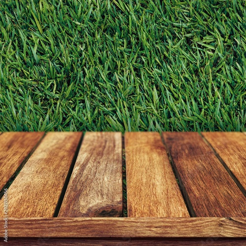 A wooden deck with a natural finish sits above lush green grass.