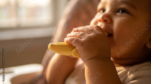 Baby smiling while grasping a yellow  silicone banana teether in a cozy indoor setting  