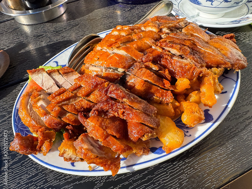 Crispy roasted duck on blue and white platter with utensils on wood surface