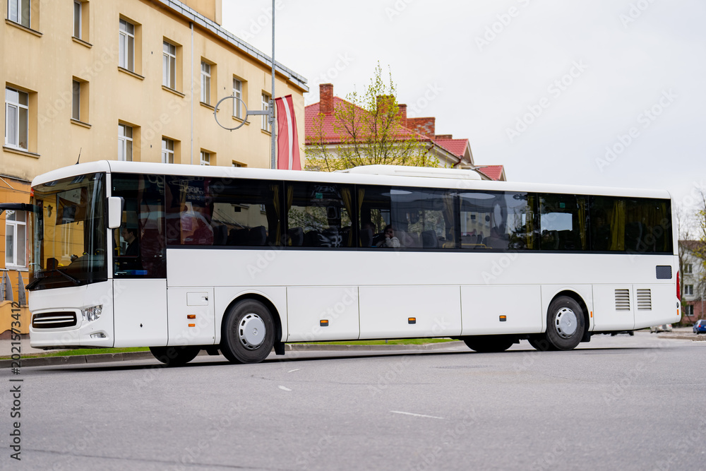 Obraz premium Large white passenger vehicle for tourism and intercity travel navigating a European town street showcasing automotive logistics and mass transport system efficiency