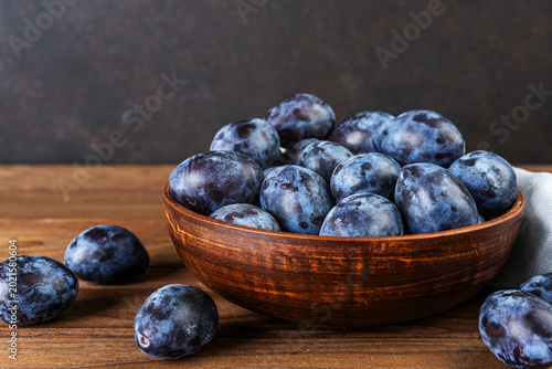 Summer harvest of sweet plums in a brown bowl over wooden surface. Healthy food concept