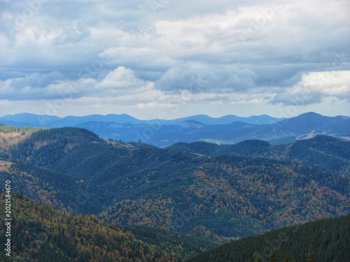 Rolling forested hills and blue mountain ranges under heavy clouds in autumn landscape