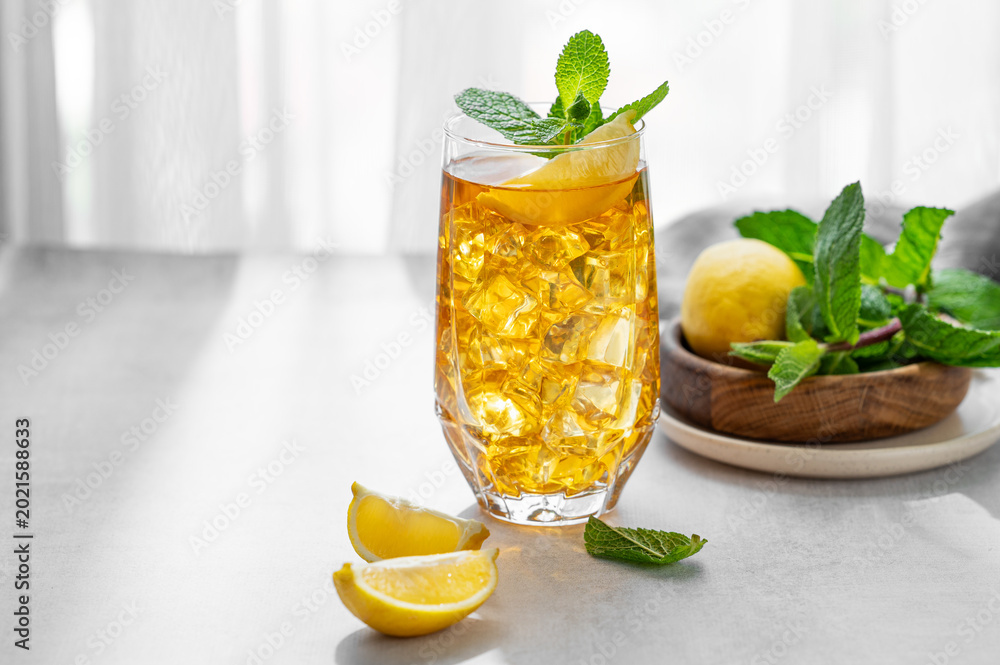 Fototapeta premium Iced tea with lemon and mint in a glass on a concrete countertop with citrus fruits