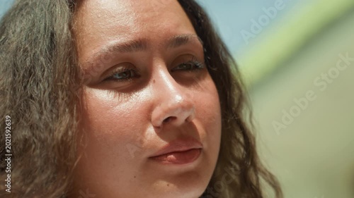 Closeup woman speaking near shore, seaside friend delivering candid monologue on island promenade, soft sunlight on face, expressive lips and eyes, casual jewelry, warm conversational mood