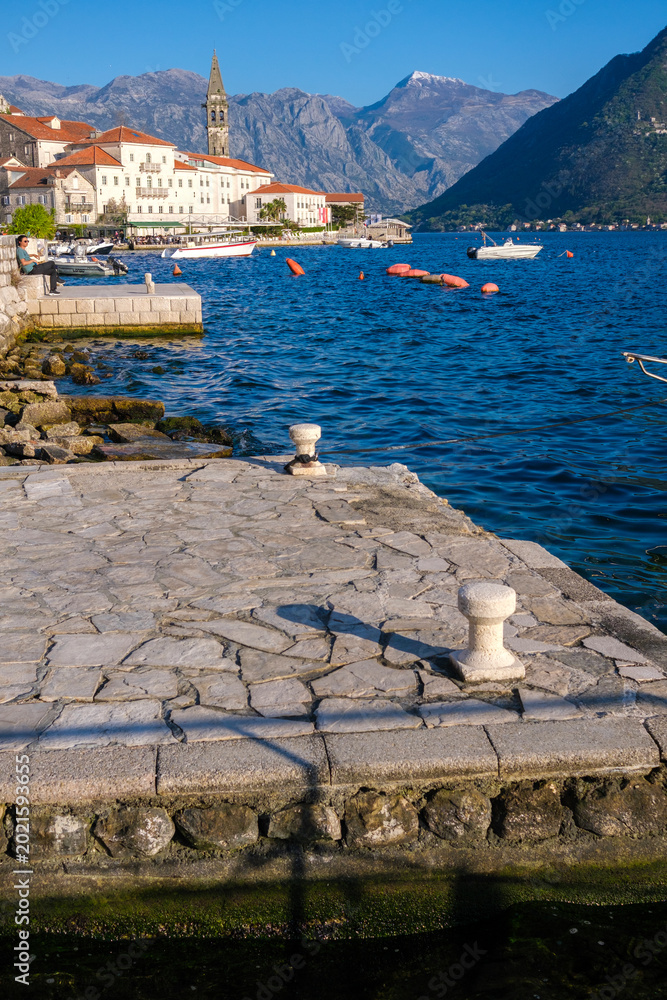 Obraz premium Visitors enjoy the serene view of Perast by the Adriatic Sea, where boats rest peacefully against a backdrop of mountains