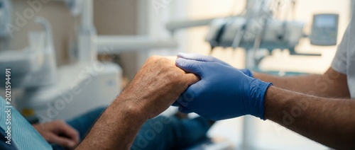 A comforting scene inside a dental clinic. A gloved professional is gently holding a patient's hand, offering a reassuring presence during the procedure.