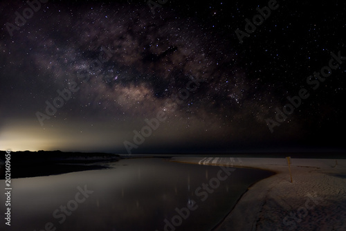 Obraz na plátně The Milky Way stretches above a quiet coastal inlet as soft reflections fade into the night