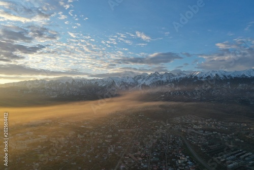 Aerial view of mountain town bathed in golden sunrise light with snow-capped peaks