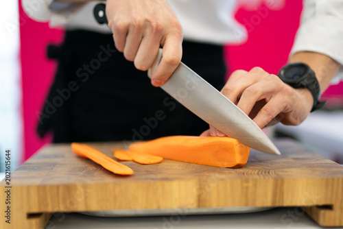Canvas-taulu Chef slicing a fresh carrot on a wooden cutting board