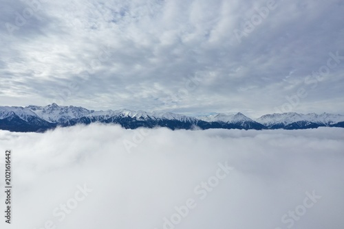 Snow-Capped Mountains Rise Above Sea of Clouds Under Overcast Sky