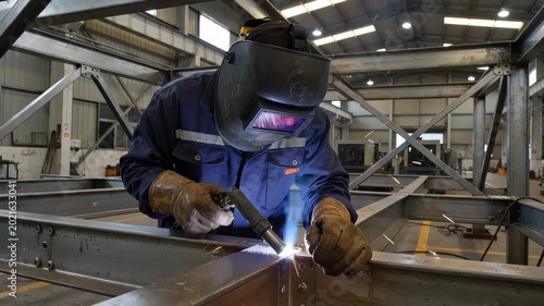 Welder in a factory working on a metal frame with sparks flying everywhere