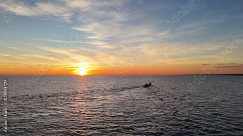 Vibrant sunset over tranquil waters with a small boat cruising in the distance