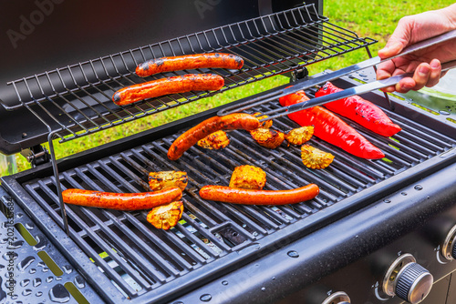 Close up view of human hand turning sausages on gas grill during outdoor cooking. Sweden.