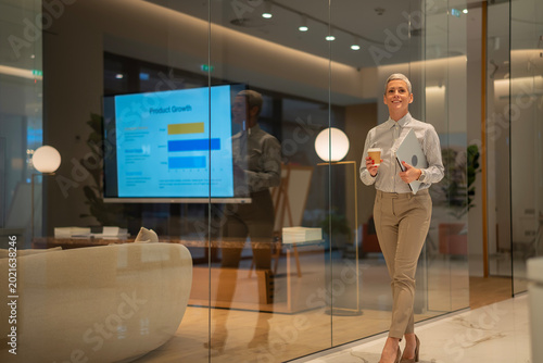 Photos Confident businesswoman walking modern office holding laptop coffee