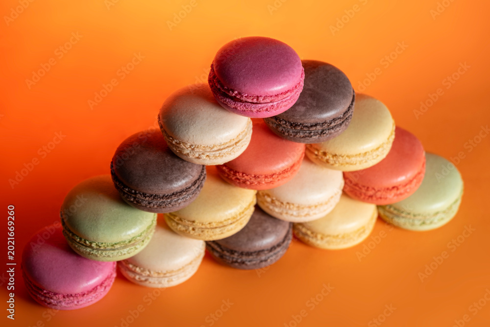 Fototapeta premium Sweet Colorful Macarons on Bright Orange Surface. Pastel Macarons Dessert Composition on Orange Backdrop. French Macarons Assorted Colors.