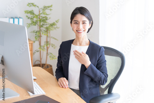 デスクトップパソコンで仕事するビジネスウーマン（胸に手を当てる）