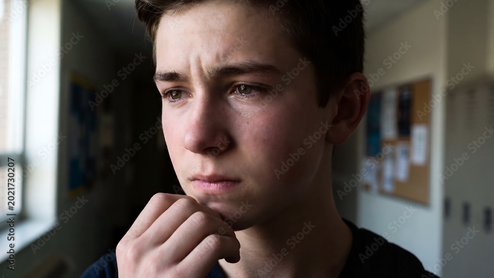 Naklejka premium Teenage boy contemplating and looking away with a pensive expression in a classroom environment