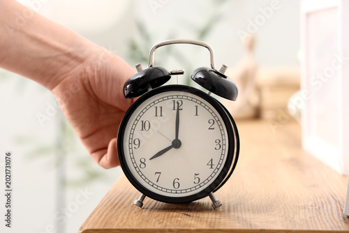 Foto Female hand setting time on alarm clock in bedroom, closeup