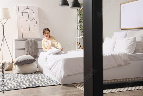 Fotografie Beautiful young woman fluffing pillows in stylish bedroom