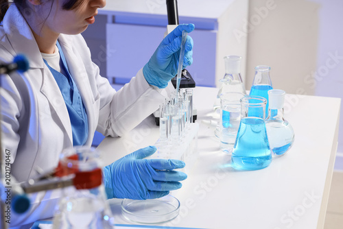 Female scientist with different flasks dropping water sample into test tube a...