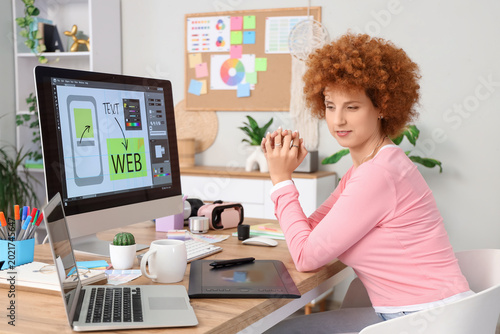 Redhead female graphic designer working at desk in office