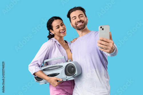 Young couple with boombox taking selfie on blue background
