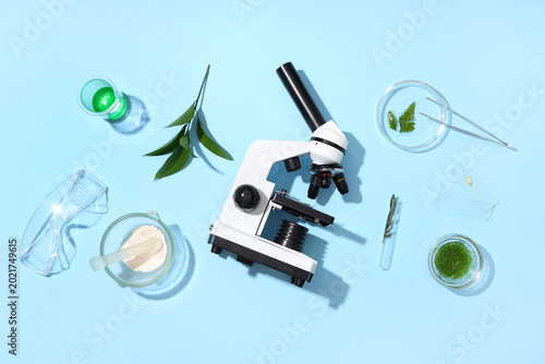 Modern microscope with different leaves, petri dish, mortar and pestle on blu...