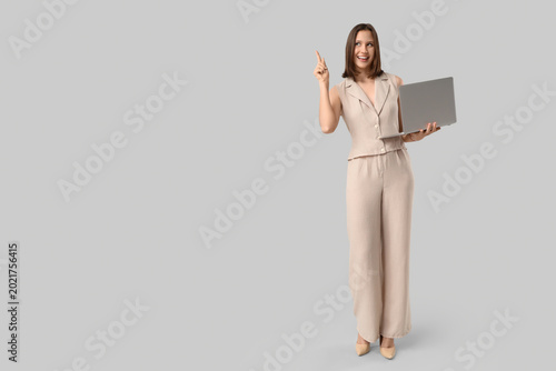 Beautiful young happy woman in stylish beige vest with laptop pointing at som...