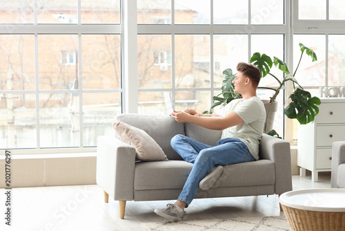 Handsome young man using laptop on sofa at home