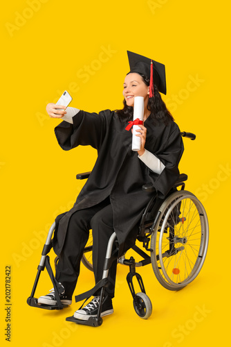 Beautiful female graduate student in wheelchair with graduation cap and diplo...