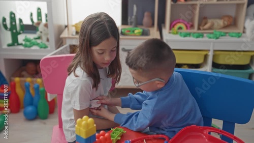 Girl and boy play doctor with toy stethoscope and place a bandage on her arm in a building; compassion imaginative play.
