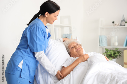 Canvas Print Female nurse putting senior woman to bed in bedroom