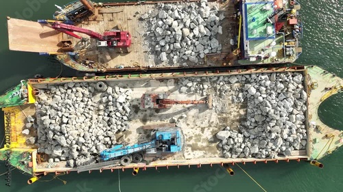 Barges with rocks ready for loading to strengthen pier at sea from Ireland by drone