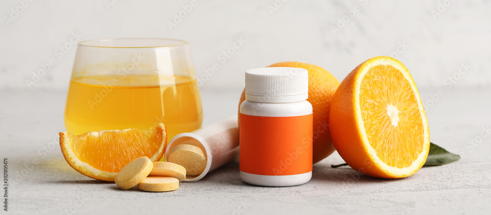 Fototapeta premium Glass of vitamin C water, pills, soluble tablets and fresh oranges on grey table