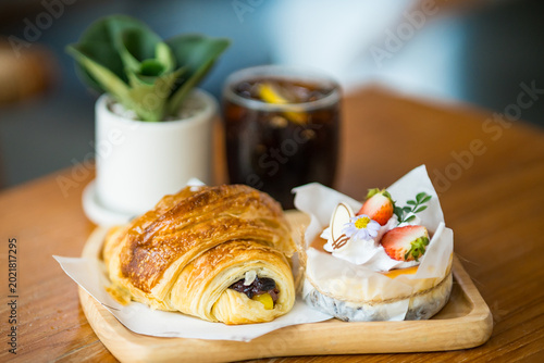 Foto Cafe Delights: A culinary moment captured, featuring a buttery croissant paired with a dainty tart, an iced beverage, and a touch of greenery, composing a tempting spread for a relaxed experience