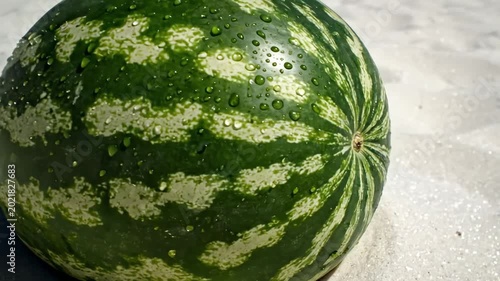 Refreshing whole watermelon with water droplets resting on tropical white sand