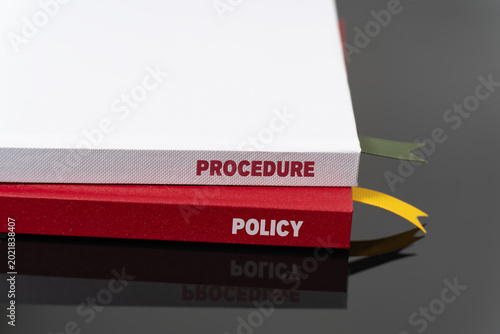 Stacked corporate handbooks titled Business and Policy on black reflective glass table