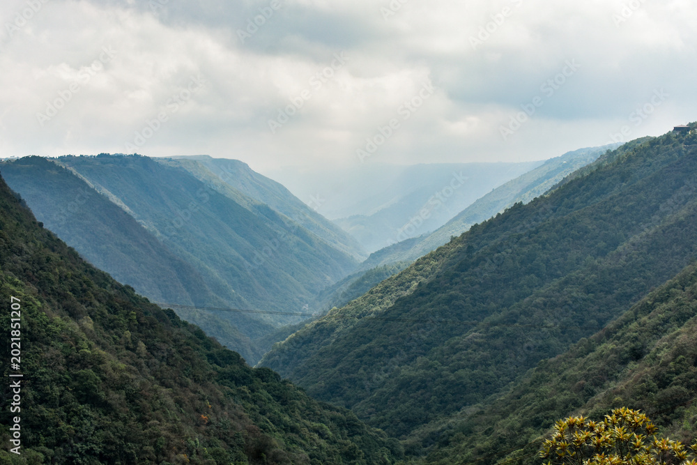 Fototapeta premium Mawkdok Dympep Valley with misty green hills and dramatic cloudy sky, showcasing breathtaking natural landscape in Meghalaya, India.