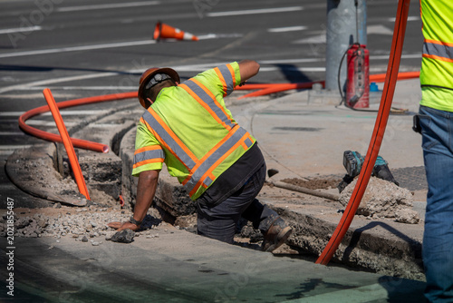 A construction worker in a trench near a large orange cable at a construction site at a street intersection